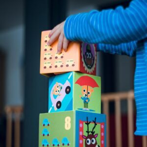A child playing indoors, stacking colorful wooden toy blocks with joyful illustrations.