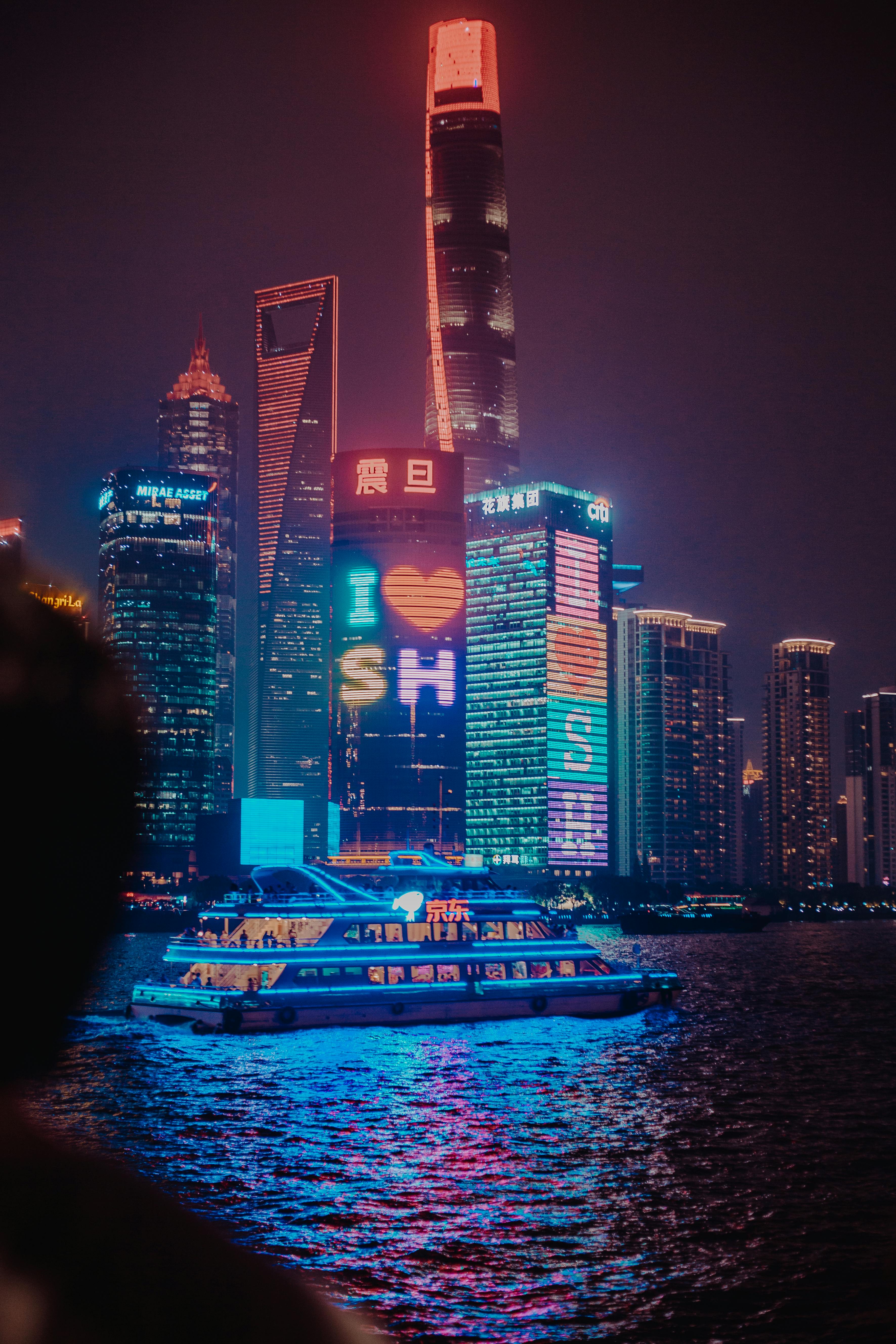 Illuminated skyscrapers with city lights reflecting in the water at night in Shanghai.