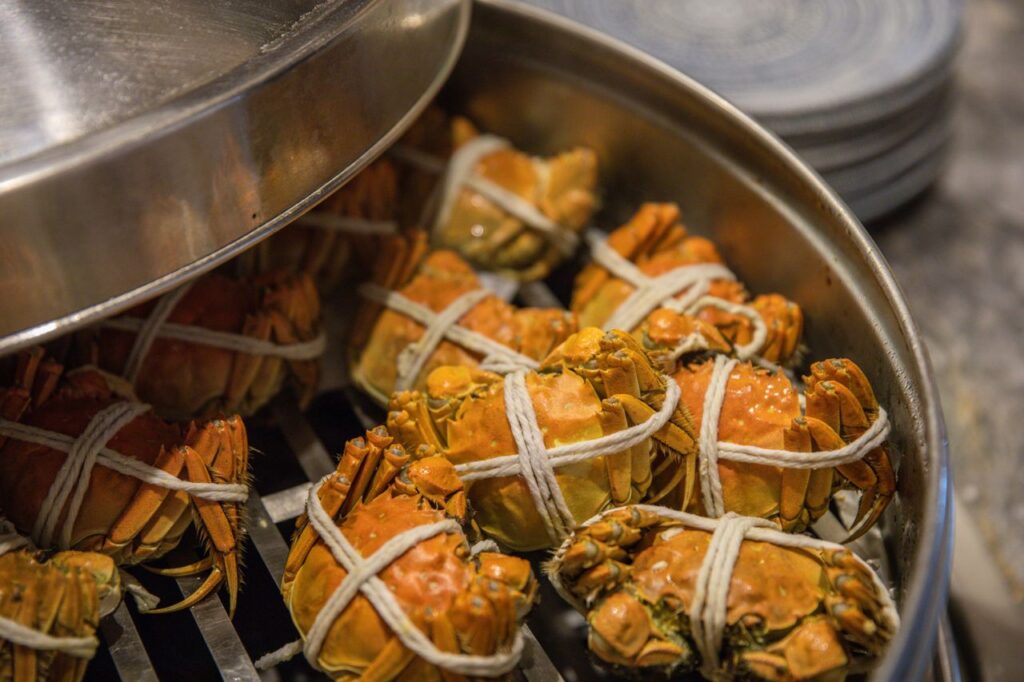 Close-up of tied crabs being steamed in a metal pot, ready for cooking.